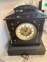 Front view of black slate and marble mantle clock with key at base
