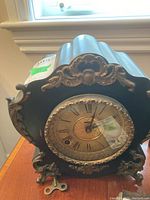 Front left view of black mantel clock showing gilt decorative mounts and winding key placed in front