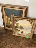 Both paintings leaning against wall, showing frontal view of each in their gilt frames