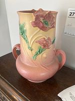 Front view of antique Roseville vase showing poppy pattern with green leaves, pink flowers on a yellow-pink shaded background, with two handles.