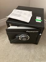 Full view of the open black SentrySafe with combination lock and attached handle. User manual placed on top of the safe.