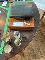 Overview of all lot items on table: boxes underneath not included in lot, two knives, sheath, crystal shakers, cups, napkin ring