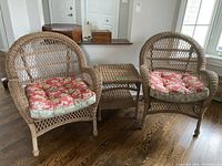 Wide view of the two wicker chairs and matching side table showing all items together with floral cushions