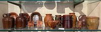 Wide view of 11 brown spatterware pieces arrayed on glass shelf