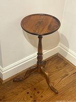 Full view of small round maple pedestal table showing top and three-legged base on wood floor.