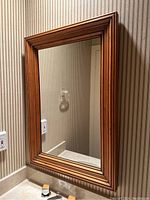 Full view of rectangular antique mirror hanging on striped wallpapered wall above a sink.