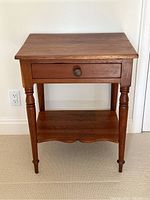 Front view of pine side table showing top, drawer, turned legs and lower scalloped shelf.