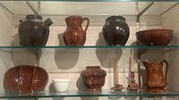 Two glass shelves displaying four pottery items on top and six on bottom in a display case