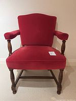 Front view of the antique red velvet armchair showing the upholstery and wooden legs.