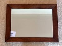 Front view of the rectangular wooden framed mirror laid flat on carpeted floor showing the reflective surface and full frame.