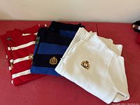 Three Ralph Lauren ladies quarter-zip sweaters folded, showing red and white striped, blue striped, and white sweaters with embroidered logos.