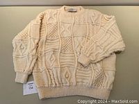 Full view of cream colored Aran fisherman’s sweater showing front and long sleeves with textured knit patterns.