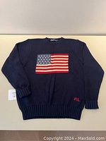 Full front view of navy sweater laid flat showing American flag design and overall condition