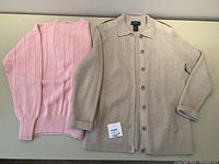 Photo of both sweaters laid flat: beige button-up cardigan and pink pullover sweater