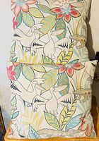 Photo showing two of the four identical accent pillows featuring pelican and floral design on light background.