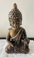 Buddha statue facing front showing detailed textured hair curls, calm face, and folded hands on lap in meditation posture