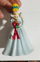 Photo of Cinderella Christmas tree ornament held in hand showing front details of the figure, gown, and bell.