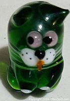 Green translucent glass cat figurine with white, black and orange painted details on the face and paws.
