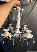 White metal chandelier with six tealight holders and clear teardrop prism decorations, held by a hand to show size and detail.