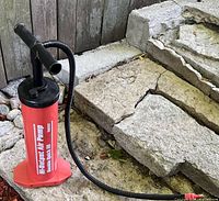 Red Intex hand-operated air pump on stone surface, showing hose and handle