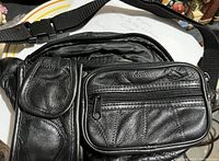Photo of the front of a black leather fanny pack showing multiple compartments and zippers with a nylon adjustable strap.