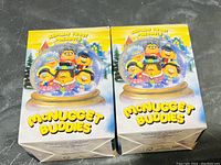 Two boxed McNugget Buddies McDonald's toys showing colorful winter-themed artwork, each box depicting six cartoon characters inside a snow globe.