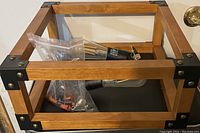 Wooden frame with black metal corners, wiring and hardware visible inside the frame on a black surface.