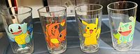Photo showing set of four clear glass tumblers with colorful Pokémon character prints of Squirtle, Charmander, Pikachu, and Bulbasaur.