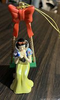 Close-up photo of Snow White Christmas tree ornament showing detailed figurine in dress and swing with red bow