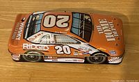 Tin keepsake box shaped like an orange Tony Stewart #20 NASCAR car with sponsorship decals.