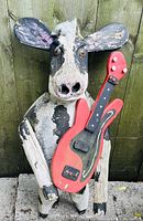 Vintage wooden cow decoration holding a red guitar, with painted features and worn paint surface.