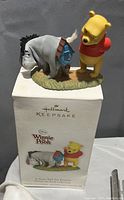 Photo of the Winnie the Pooh and Eeyore ornament displayed on top of its original Hallmark Keepsake box. Box shows ornament name and branding.