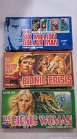 Three game boxes for The Six Million Man, Bionic Crisis, and The Bionic Woman are stacked horizontally on a white background.