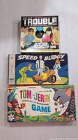Top view of all three vintage board game boxes stacked: Trouble, Speed Buggy, Tom and Jerry Adventures in Blunderland