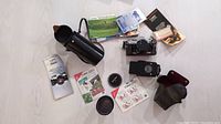 Complete lot including Canon AE-1 camera with 50mm lens attached, Vivitar 70-210mm lens, camera and lens cases, flash unit, booklets, and promotional materials spread on floor.