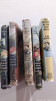 Five Hardy Boys books in a row showing their dust jackets' spines and some cover wear.