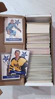 Box with large stack of hockey cards and three cards individually sleeved featuring Frank Mahovlich, Stan Mikita, and Charlie Hodge.