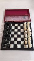 Full view of chessboard with all chess pieces set up and red velvet storage case open behind
