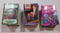 Three stacks of Nancy Drew paperback books showing illustrated covers from various series and years.