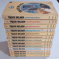 Stack of 13 Trixie Belden paperback books showing spines with volume numbers and titles.