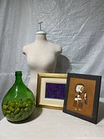 Photo showing sewing mannequin torso, two framed artworks, and green glass bottle with corks