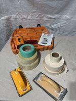 Photo showing laser level inside orange hard case with user manual and accessories, plus drywall mesh tapes and sanding blocks on table.