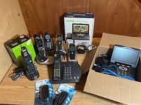 Photo showing multiple cordless and corded landline phones placed on wooden surface along with two boxed phones and associated power cords and accessories.