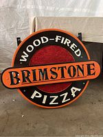 Front view of the circular Brimstone Wood-Fired Pizza wooden sign with black, orange, and red color scheme and raised lettering.