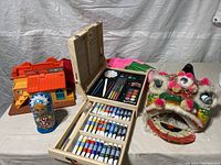 Various toys and art supplies including a vintage playhouse, matryoshka doll, wooden art kit, and lion dance mask displayed on table.