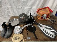 Full lot view showing boots, skateboard, pans, cooler bag and other items arranged on table