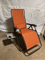 Front view of the reclining lawn chair with orange fabric, metal frame, armrests, and side table.