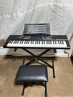Front view of RockJam electric keyboard on adjustable X-frame stand with padded bench in front.