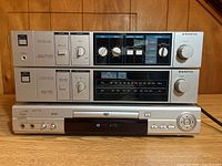 Front view stacked view showing Sanyo System 220 integrated amplifier and tuner stacked on top of Malata DVP-310 DVD player, silver finish, various knobs and buttons.