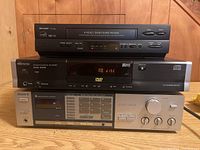 Front view of Sharp VC-A560 VCR, Memorex MVD-2025 DVD player, and Sony STR-VX33 receiver stacked on wooden surface.